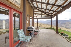 A covered patio with a view of mountains, a grill, and a chair. - Hot Tub, Valley Views & 40 Acres in Methow (Pateros)