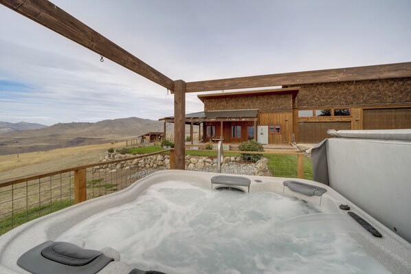 A hot tub area with a view of a wooden building and mountains in the background.