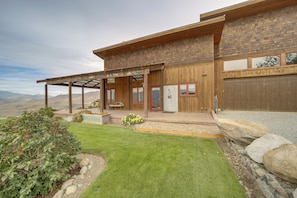 A modern two-story house with a covered patio, a stone retaining wall, and a well-maintained lawn.