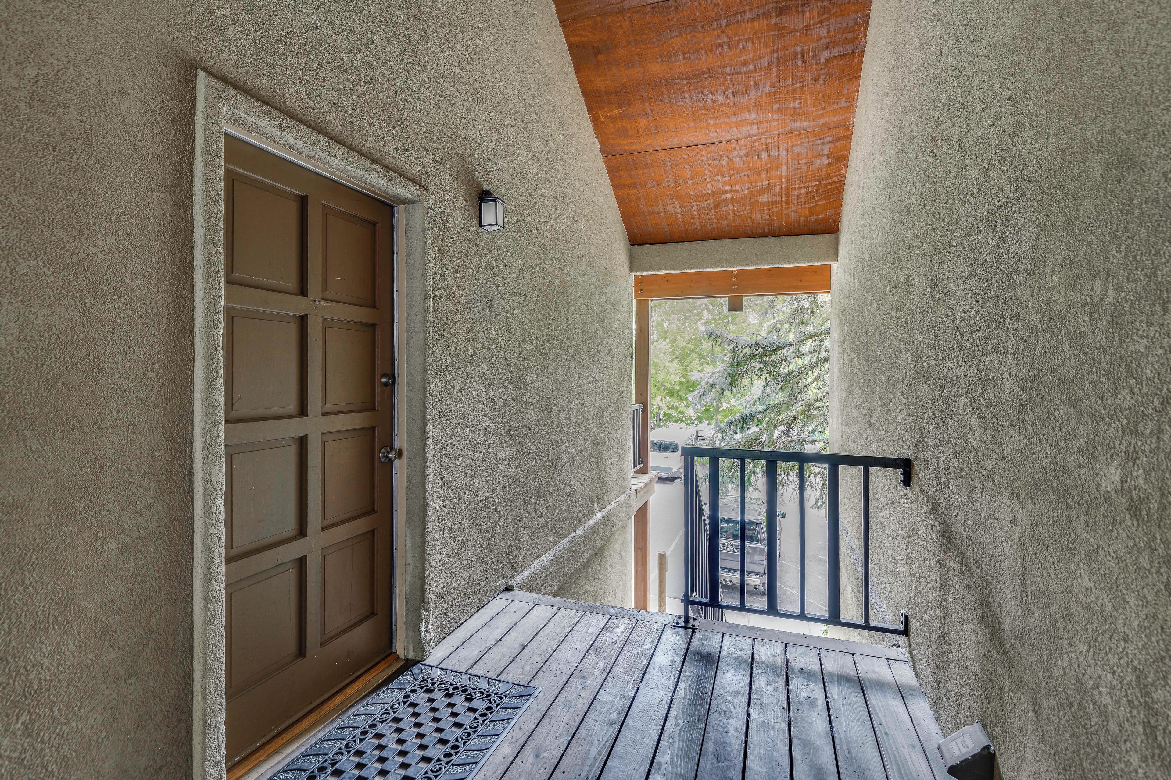 A covered outdoor area with a wooden door, a metal railing, and a view of the street.