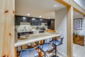 A kitchen with dark cabinets, a white countertop, and a bar area with two bar stools. - Walk to Ski Slopes! Sun Valley Condo w/ Balcony (Ketchum)