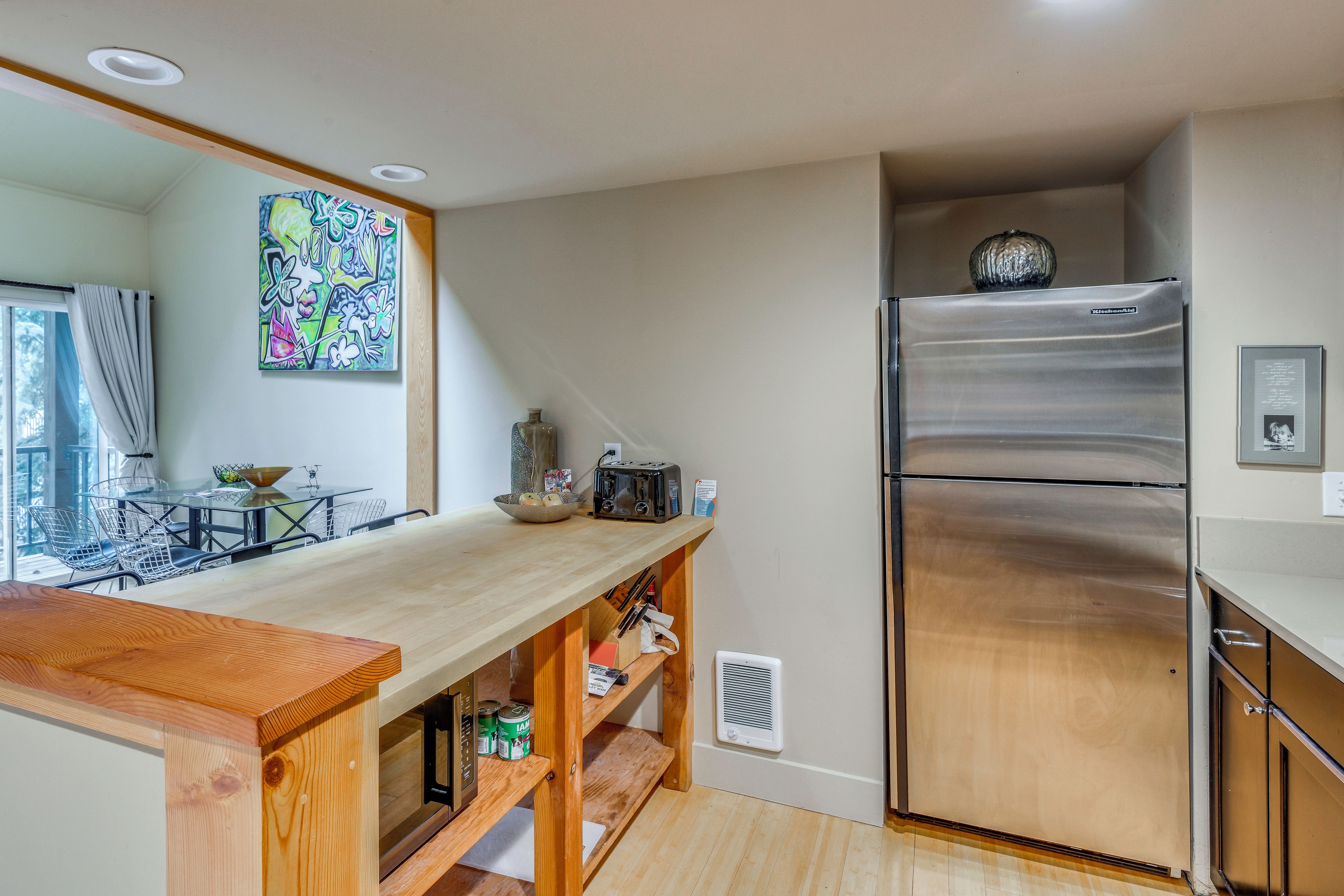 A modern kitchen with a wooden countertop, stainless steel refrigerator, and a dining area with a glass table and chairs.