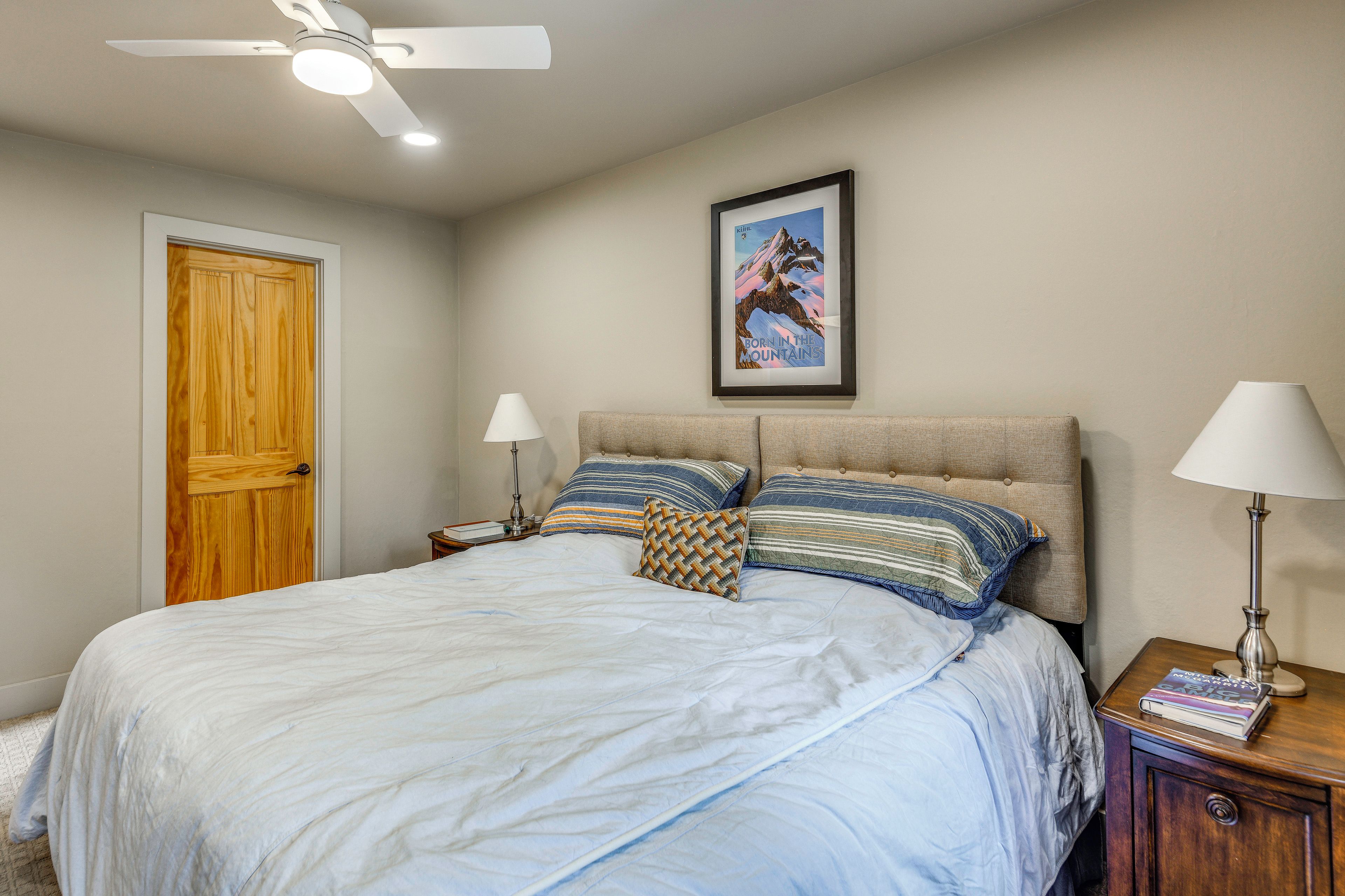 A bedroom with a bed, two bedside lamps, a framed picture on the wall, and a ceiling fan.