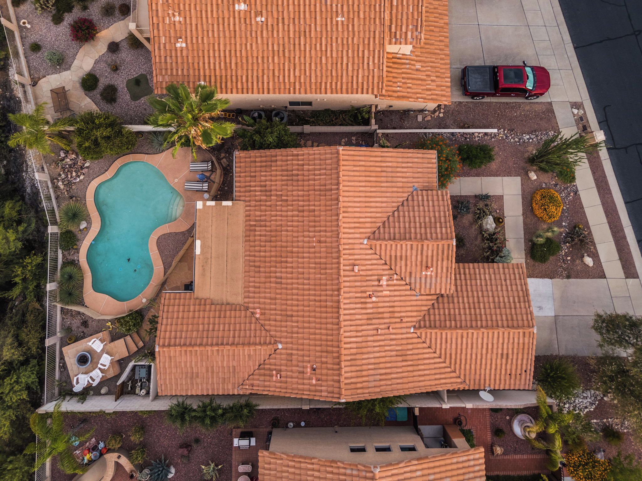 A residential area with a swimming pool, patio furniture, and a red car parked on the street.