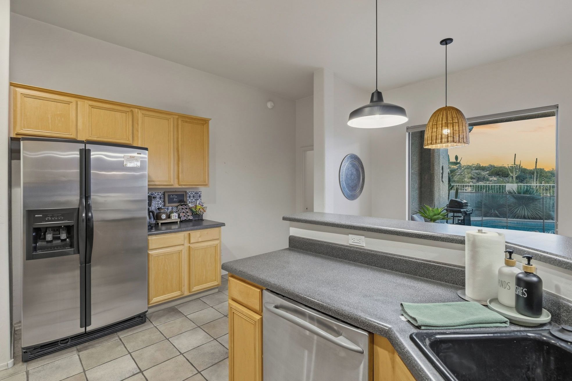A modern kitchen with stainless steel appliances, wooden cabinets, a granite countertop, and a view of a pool.