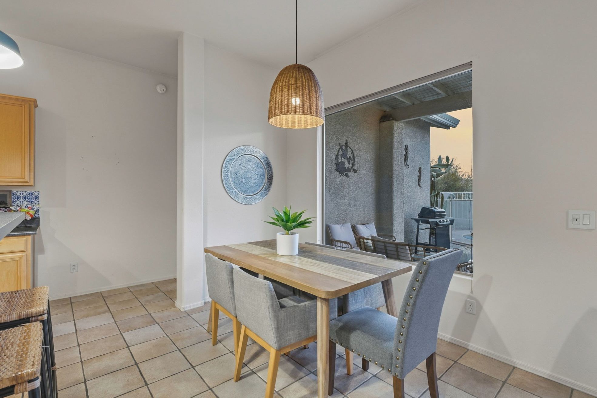 A dining area with a wooden table, grey upholstered chairs, a hanging pendant light, a potted plant, and a decorative plate on the wall.