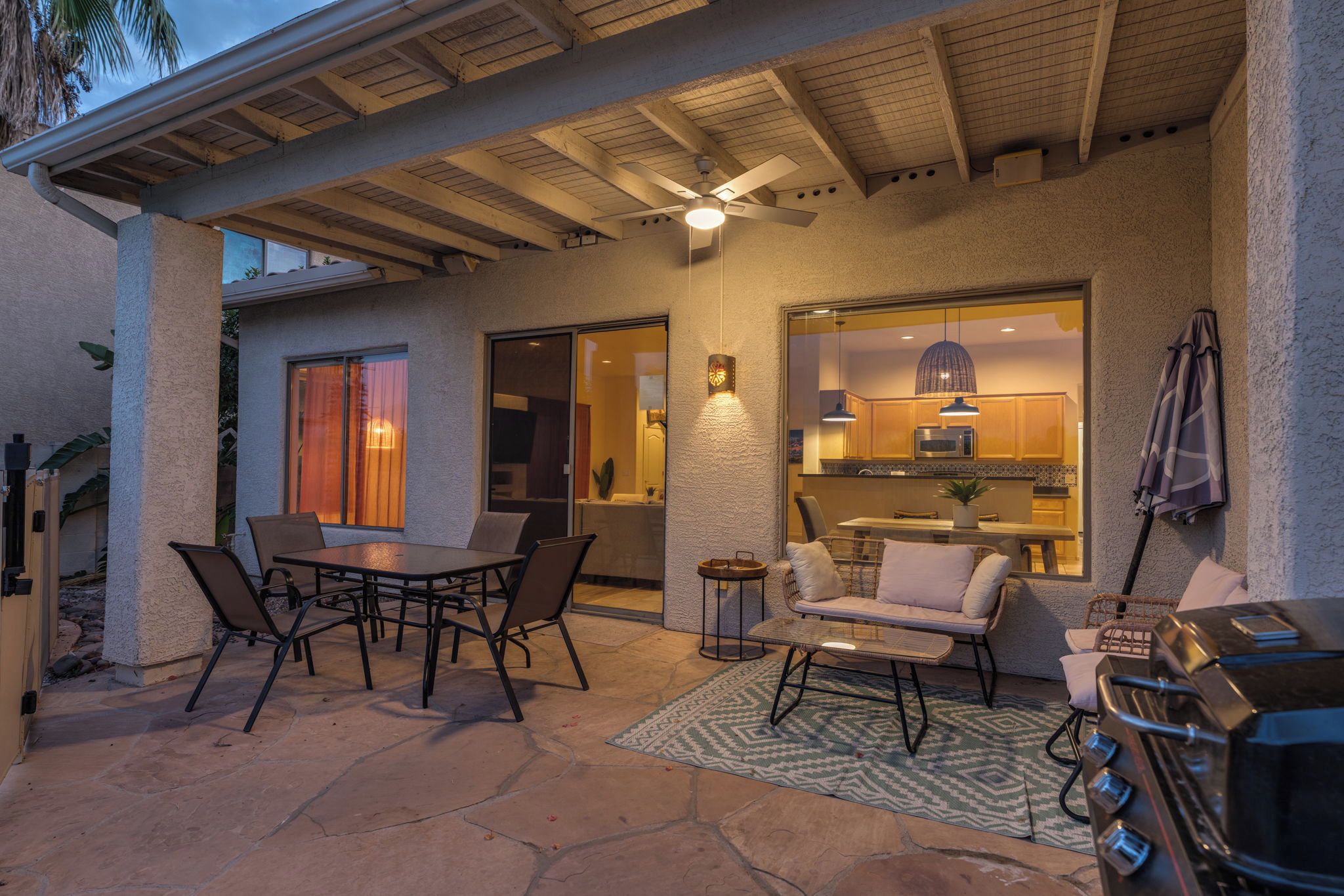 An outdoor patio area with a dining table and chairs, a grill, and a kitchen visible through an open door.