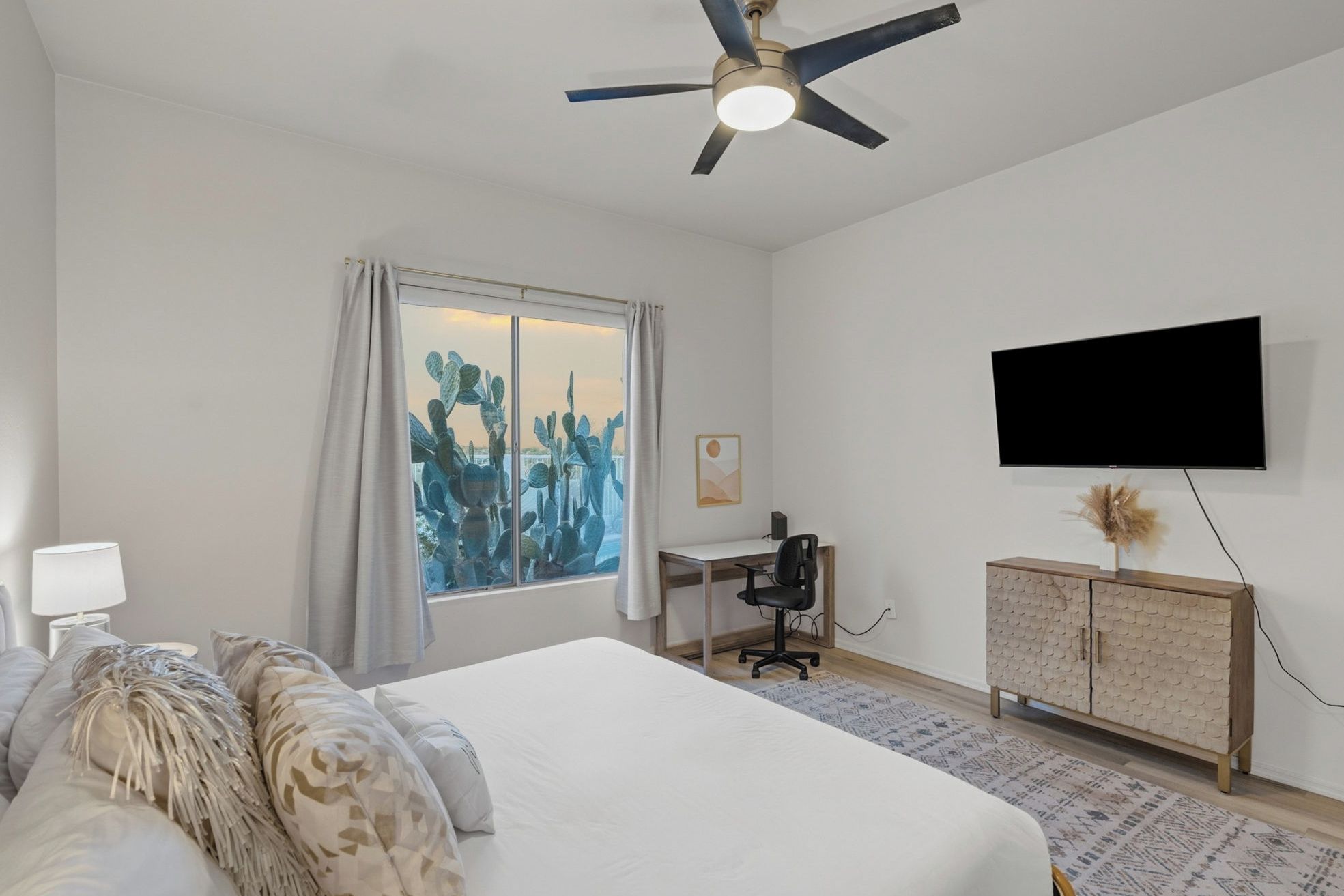 A bedroom with a bed, a desk, a chair, a television, and a ceiling fan.