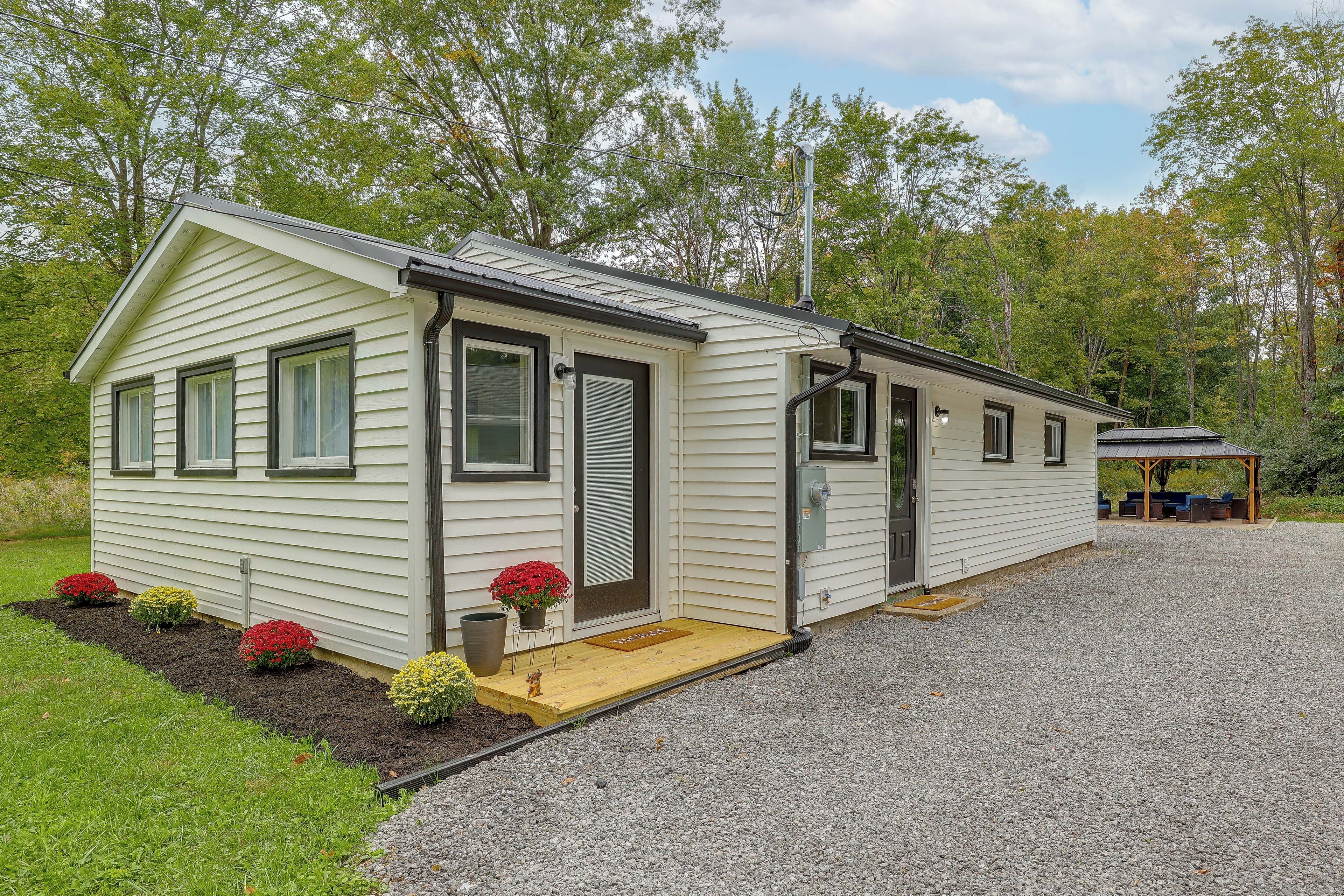 A single-story mobile home with a front porch, a covered outdoor seating area, and a gravel driveway.