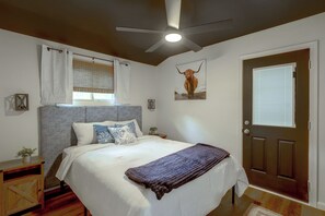 A bedroom with a bed, a ceiling fan, a door, and a window with blinds.