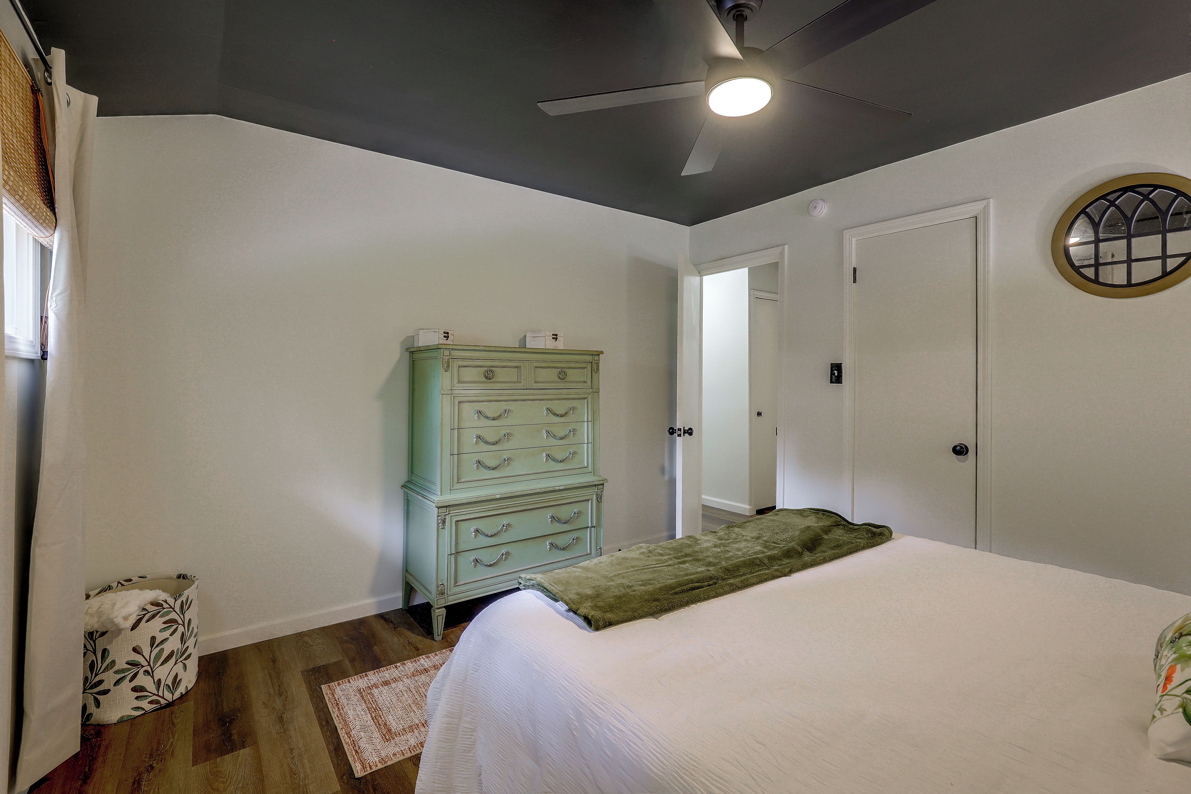 A bedroom with a bed, a dresser, a ceiling fan, and a door.