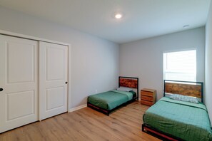 Ein Schlafzimmer mit zwei Einzelbetten, einer Holzkommode, einem Fenster mit Jalousien und einer weißen Tür.