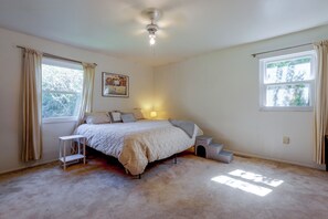 Ein Schlafzimmer mit Bett, Nachttisch, Lampe, Fenster und Deckenventilator.