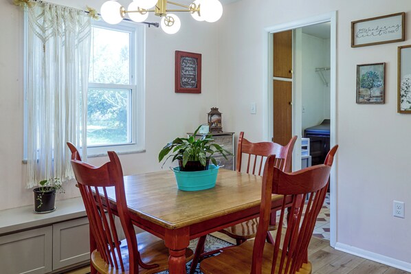 A dining area with a wooden table and chairs, a potted plant, and a wall with framed artwork.