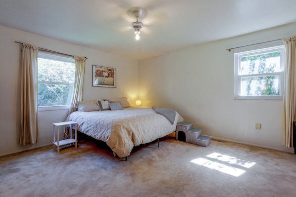 Un dormitorio con cama, mesita de noche, lámpara, ventana y ventilador de techo.