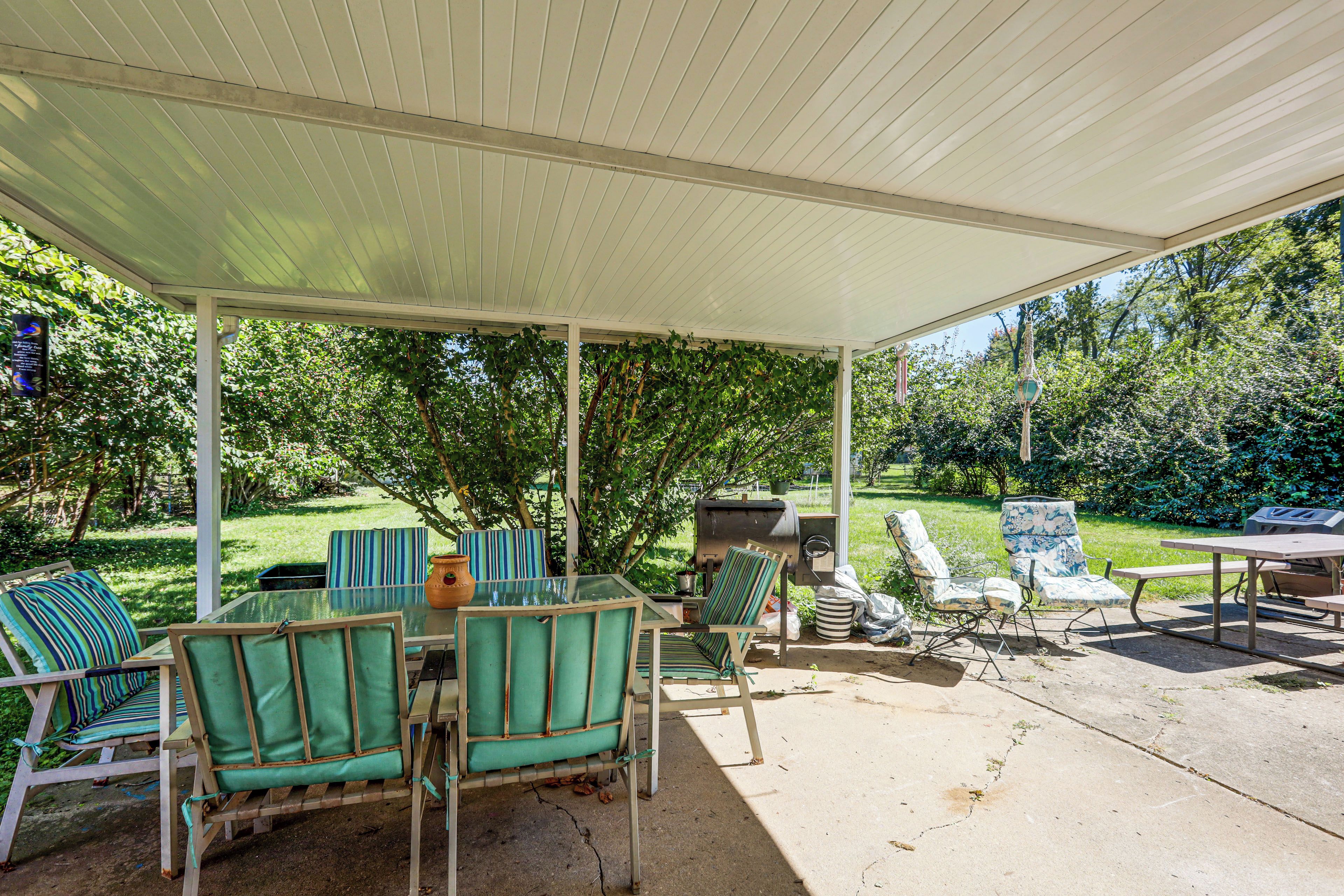 Une terrasse extérieure dotée d’un espace salon abrité, d’un barbecue et offrant une vue sur un jardin luxuriant.