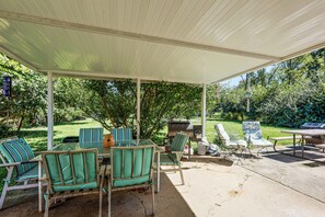 Eine Terrasse im Freien mit überdachter Sitzgelegenheit, einem Grill und Blick auf einen üppigen Garten.