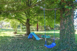 A playground with a swing set and a slide, surrounded by trees and grass. - Dayton Area Extended Stay w/ Half-acre Garden (Dayton)