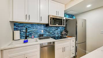 A modern kitchen with white cabinets, a stainless steel dishwasher, a microwave, and a refrigerator.