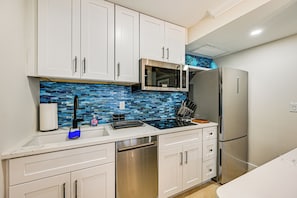 Una cocina moderna con armarios blancos, lavavajillas de acero inoxidable, microondas y refrigerador.