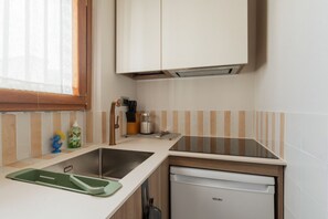 A compact kitchen with a dishwasher, a sink, and a window with blinds. - A cozy and bright 35 square-meter apartment, ideal for two people, located on the fifth floor of a building (elevator up to the third floor and is accessible only after a few steps; NOT suitable for people with disabilities) in a quiet, well-connected re (Milan)