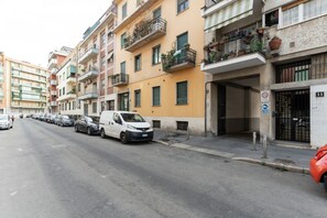 A street with parked cars and a white van. Buildings line the street, some with balconies and plants. - A cozy and bright 35 square-meter apartment, ideal for two people, located on the fifth floor of a building (elevator up to the third floor and is accessible only after a few steps; NOT suitable for people with disabilities) in a quiet, well-connected re (Milan)