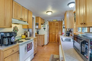 A kitchen with wooden cabinets, a stove, a coffee maker, and a microwave. - Upscale Beachfront Log Home on Lake Huron Shores (Drummond Island)