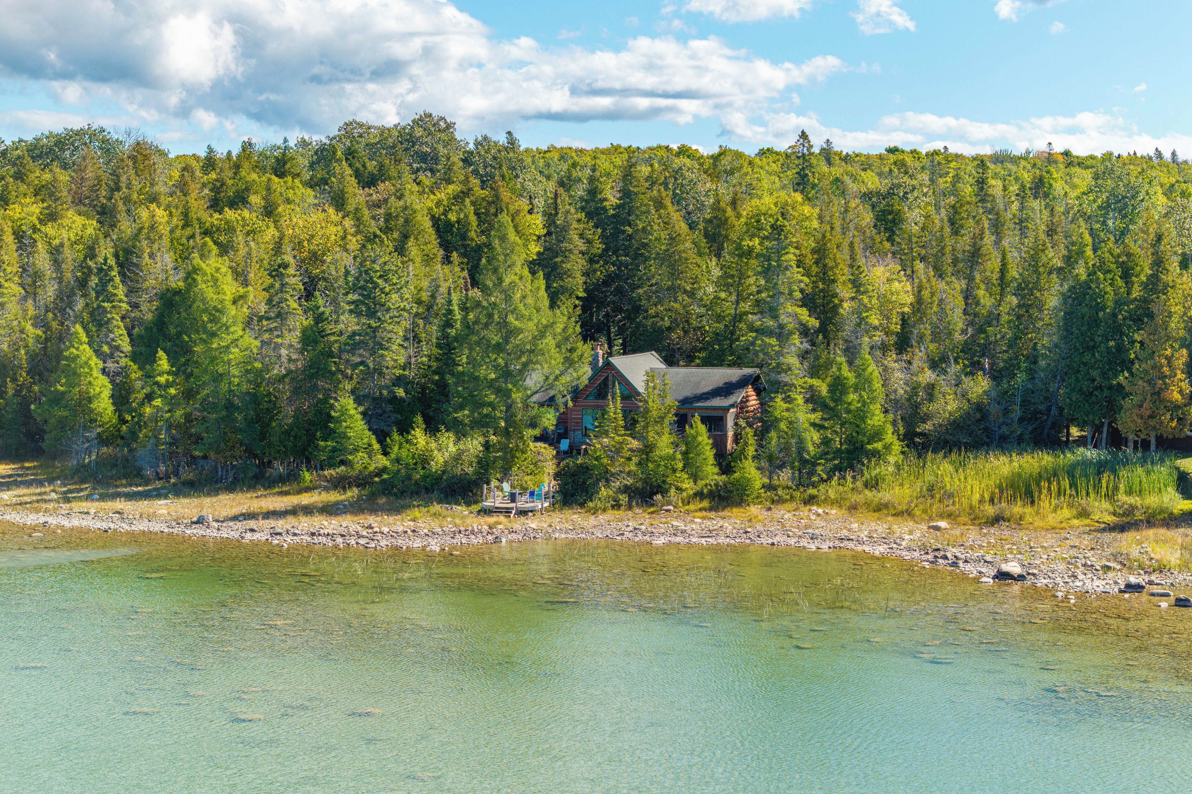 A cabin by a lake with a dock and chairs.