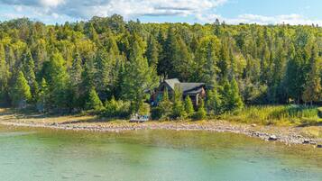 A cabin by a lake with a dock and chairs.