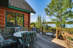 Una cabaña de madera con terraza, mobiliario exterior y vista a un lago.