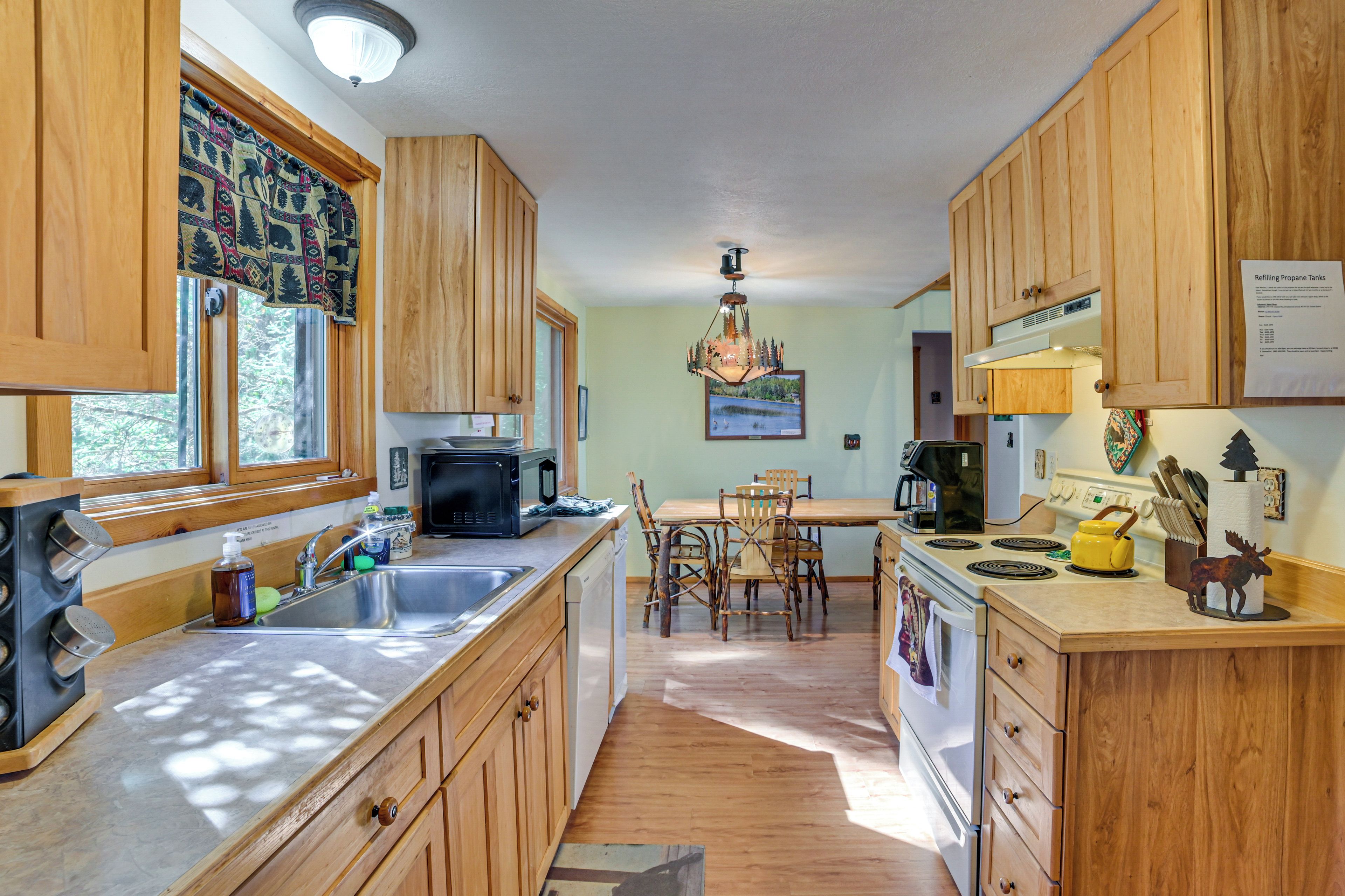 A kitchen with wooden cabinets, a microwave, a sink, and a dining area with chairs.