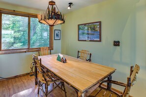 A dining area with a wooden table and chairs, a chandelier, and framed pictures on the walls. - Upscale Beachfront Log Home on Lake Huron Shores (Drummond Island)