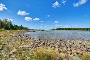 A lakeside view with a rocky shoreline, calm water, and a clear sky. - Upscale Beachfront Log Home on Lake Huron Shores (Drummond Island)