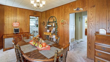 A dining room with a wooden table, chairs, a chandelier, and a kitchen in the background.