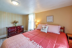 A bedroom with a bed, dresser, lamp, and a framed picture on the wall.