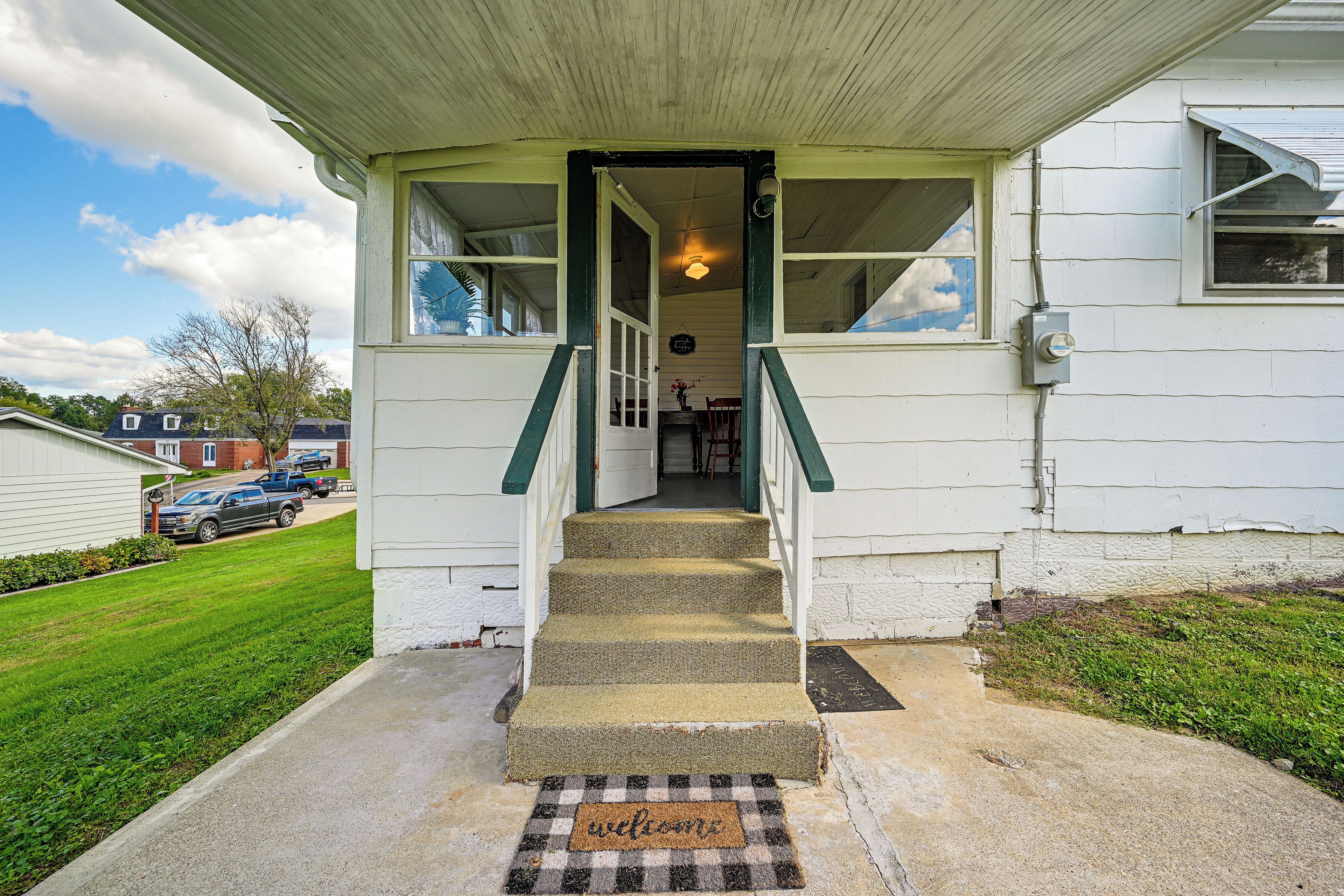A house with a front porch, a set of stairs leading to the entrance, and a doormat with the word 'welcome'.