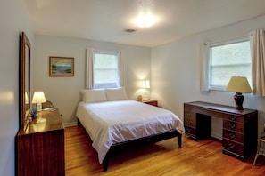 A bedroom with a bed, a dresser, a nightstand, a lamp, a painting, and a window with blinds. - Dog Friendly & Vintage Vibe! 13 Mi to St Simons (Brunswick)
