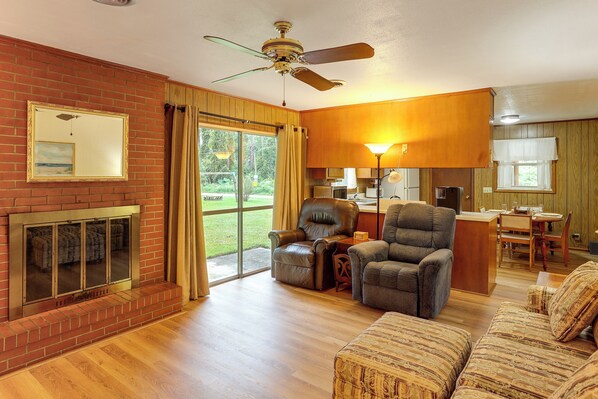 A living room with a fireplace, a ceiling fan, and a dining area with a kitchen in the background. - Dog Friendly & Vintage Vibe! 13 Mi to St Simons (Brunswick)