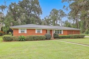 A single-story brick house with a gabled roof, a front porch, and a well-maintained lawn. - Dog Friendly & Vintage Vibe! 13 Mi to St Simons (Brunswick)