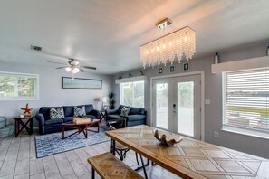 A modern living room with a blue sofa, a wooden dining table, and a ceiling fan. - Game Room & Hot Tub! Bayfront Family Gem (Fort Walton Beach)