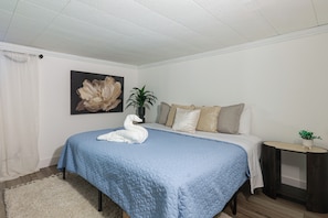 Quarto com cama, almofadas, mesa de cabeceira, planta e quadro na parede.