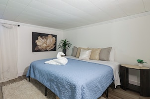 Quarto com cama, almofadas, mesa de cabeceira, planta e quadro na parede.