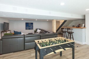 Uma sala de estar moderna com sofá seccional, mesa de pebolim e parede de tijolos.