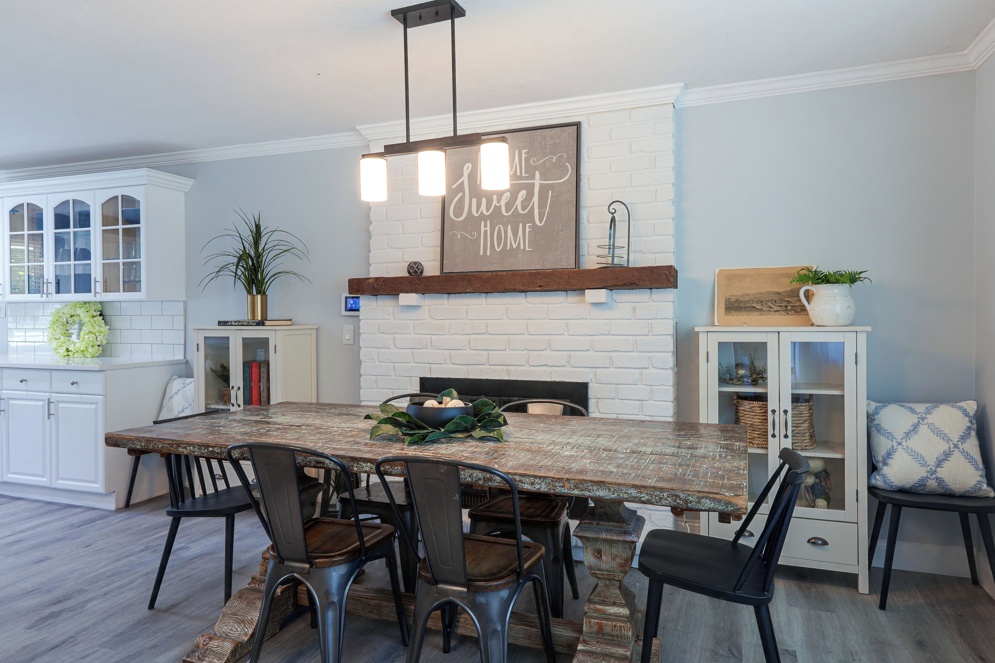A dining area with a large wooden table, black chairs, and a white brick fireplace.