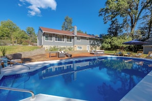A residential property with a swimming pool, outdoor furniture, and a house with a red roof.