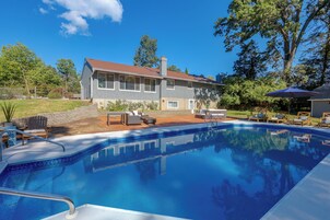 Um imóvel residencial com piscina, móveis de exterior e uma casa com telhado vermelho.