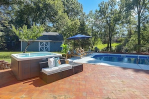 A backyard with a hot tub, a pool, and outdoor seating.