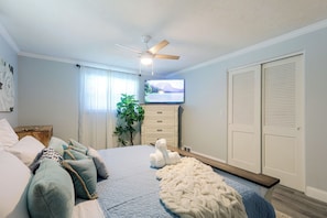 A bedroom with a bed, a TV, a ceiling fan, a plant, and a wardrobe.