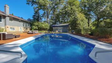 A swimming pool with a clear blue water surface, surrounded by a patio area with outdoor furniture.