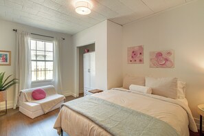 Ein Schlafzimmer mit einem Bett, einem Fenster mit Vorhängen, einem Nachttisch und einer Wand mit zwei Bildern.